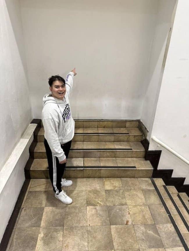 Smiling man pointing at one of the boldest construction fails, a staircase into a wall.