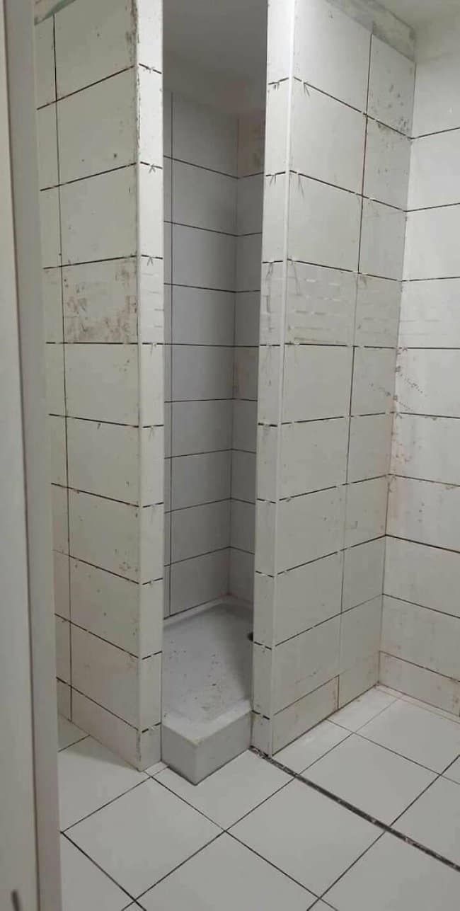 Tiled shower stall so narrow a person would have to enter sideways.