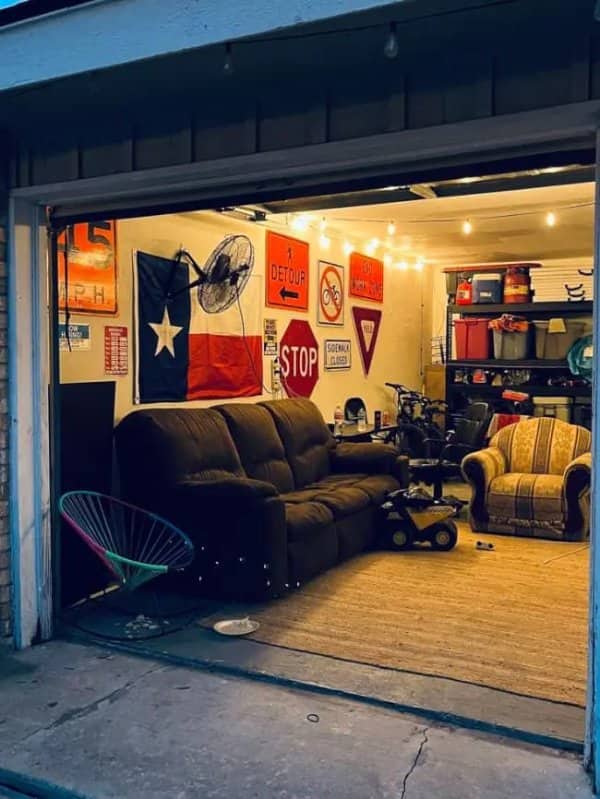 Open garage man cave with a Texas flag, road signs, string lights and a brown couch