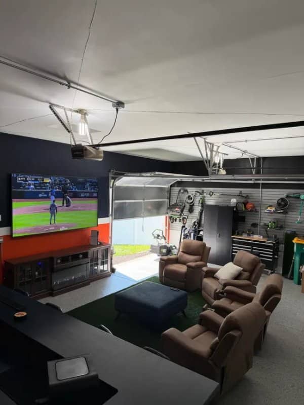 Garage converted into a lounge with a large television, recliners and green turf flooring