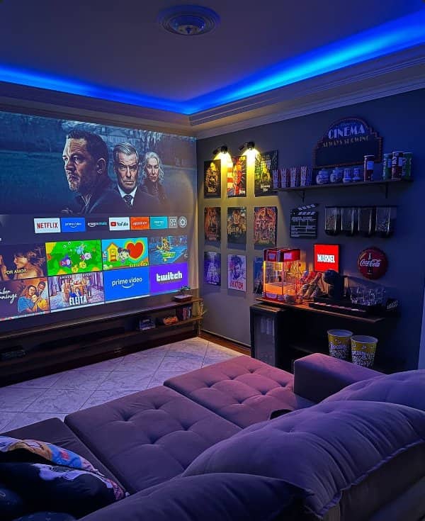 Home cinema room with a projector screen, blue ceiling lighting, movie posters and popcorn machine
