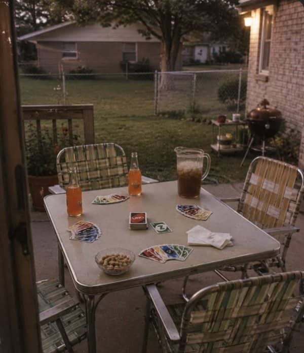 Backyard patio table at dusk set with Uno cards, iced tea and aluminum lawn chairs