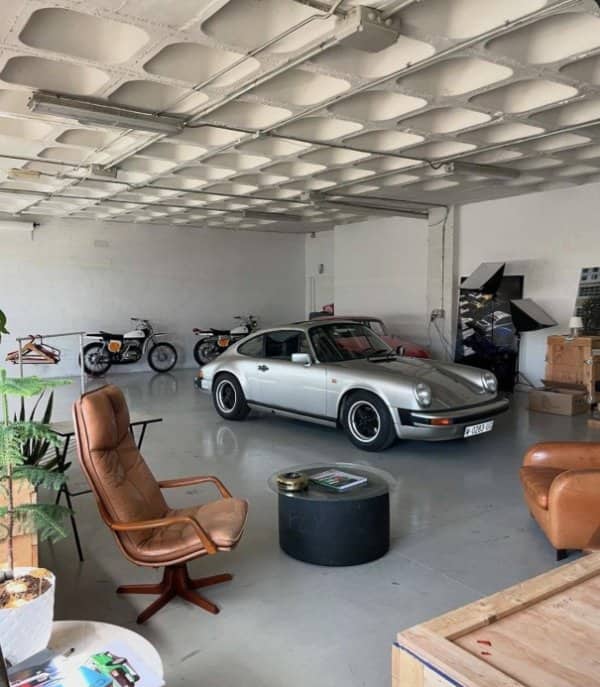 Spotless garage housing a silver Porsche, two vintage motorcycles and a leather lounge chair