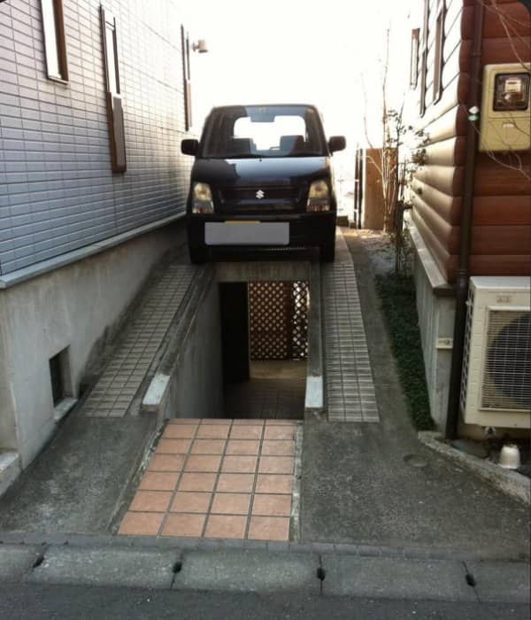 Small car parked on a platform above a narrow sunken stairway leading to a basement room