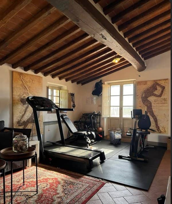 Home gym under exposed wooden beams with a treadmill, exercise bike and Da Vinci prints