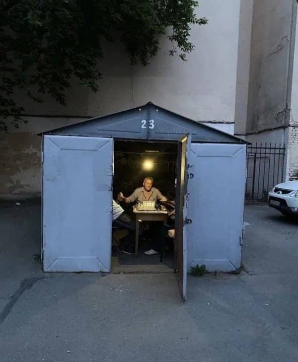 Man sitting at a small desk inside a tiny metal garage with the doors propped open