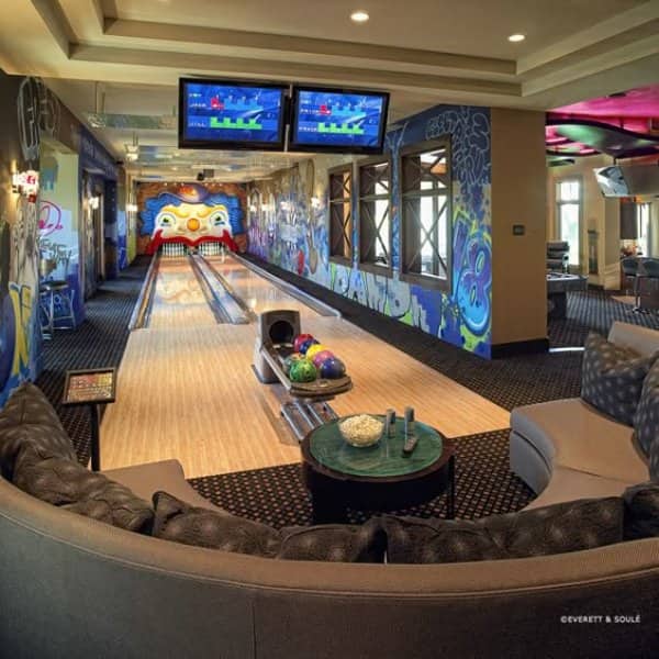 Private basement bowling alley with two lanes, graffiti murals, screens and a curved sofa