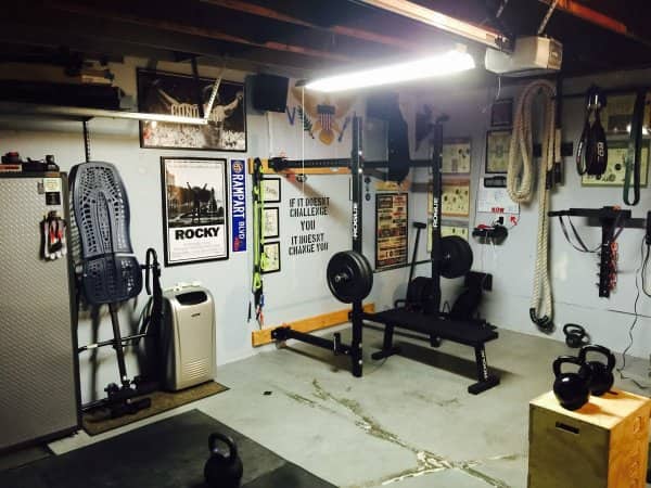 Basement home gym with a bench press, kettlebells, climbing rope and a Rocky poster