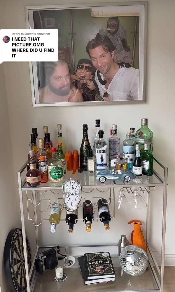 Home bar cart loaded with spirits under a framed photo from a comedy movie