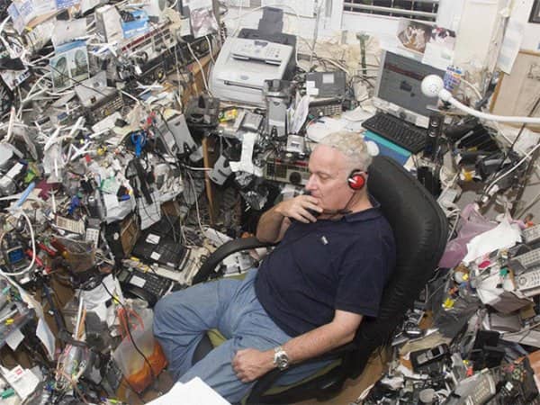 Man reclining in an office chair completely surrounded by stacked radios, phones and tangled cables