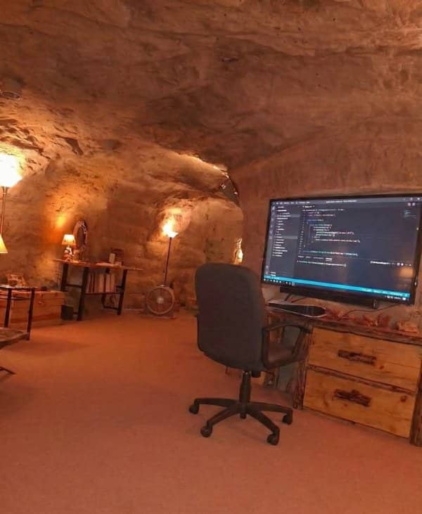 Office carved into a sandstone cave with a monitor, rolling chair and warm lamps