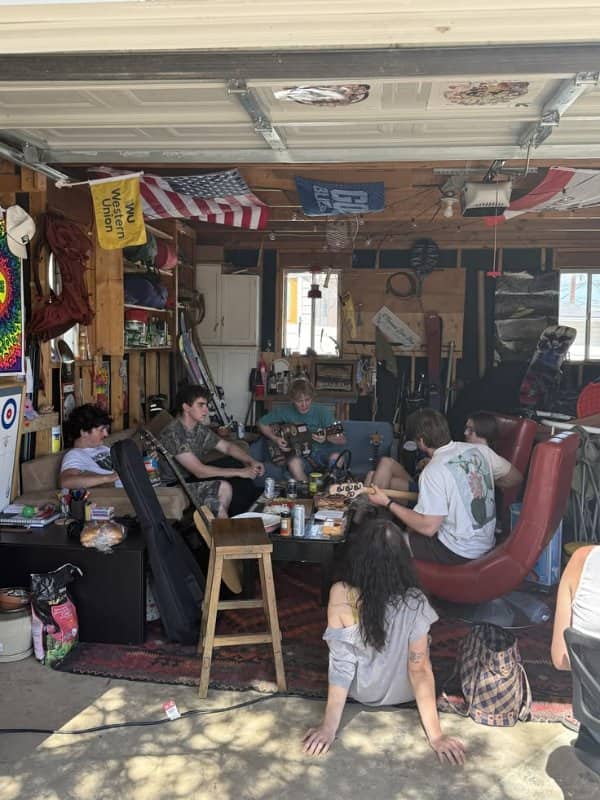 Friends hanging out in a garage with guitars, flags, snacks and mismatched thrifted furniture