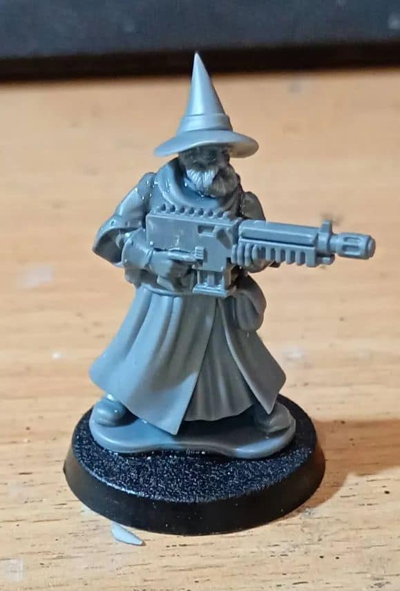 Unpainted gray miniature of a pointed hat wizard holding a large futuristic rifle.