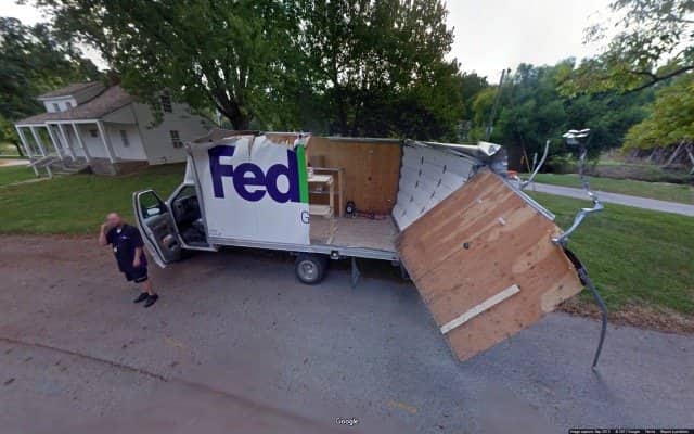 Delivery driver on the phone beside his box truck, its cargo body ripped wide open.