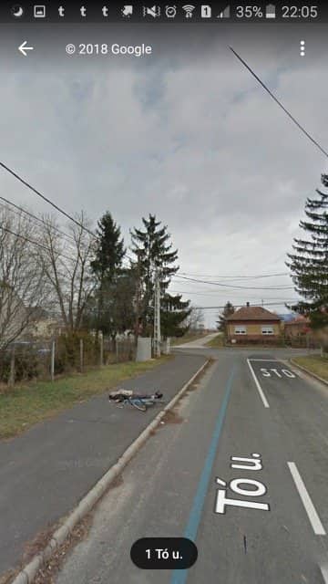 Person lying on a quiet village road next to a bicycle, caught on Google Street View.