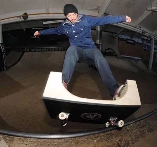 Skateboarder grinding on a mini ramp shaped like a miniature skate park ramp.