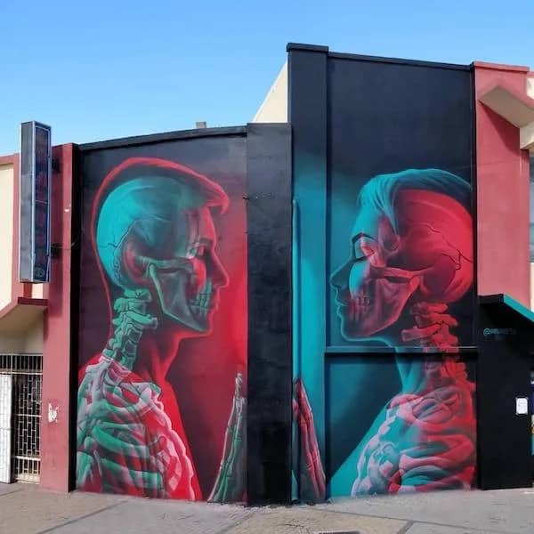 Vibrant street art mural showing two transparent colorful skeleton figures facing each other.