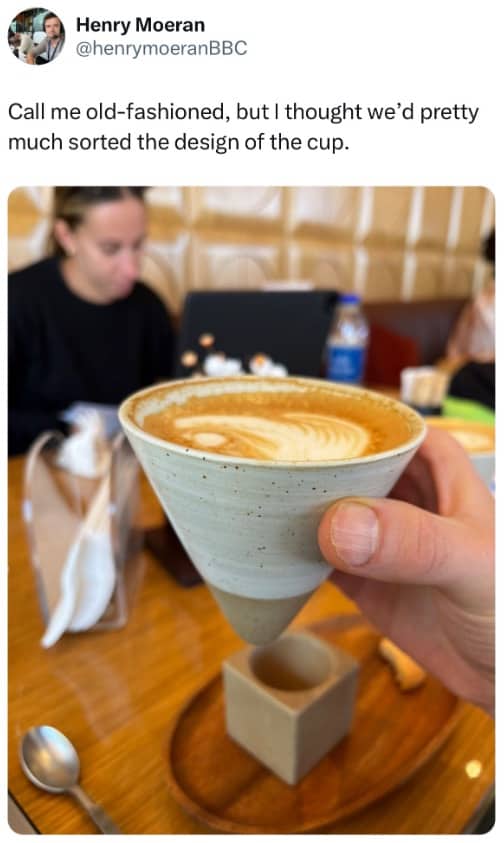 Person holding cone shaped coffee cup that cannot stand up without its wooden holder.