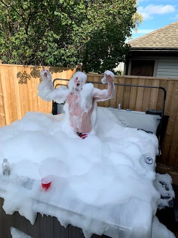 Person covered in thick white foam posing inside overflowing outdoor hot tub.