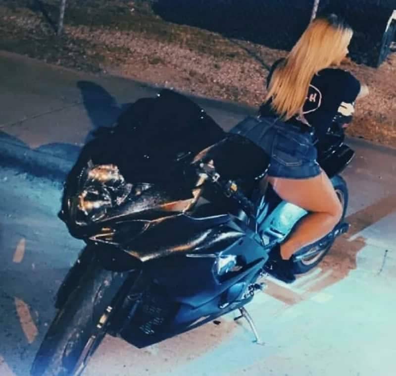 Woman awkwardly posing on a parked motorcycle at night displaying obvious main character syndrome energy.