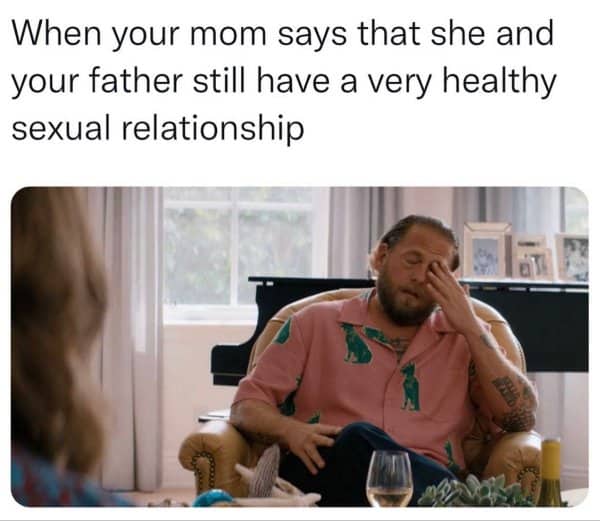 Man in a patterned shirt winces in an armchair after hearing too much from mom.
