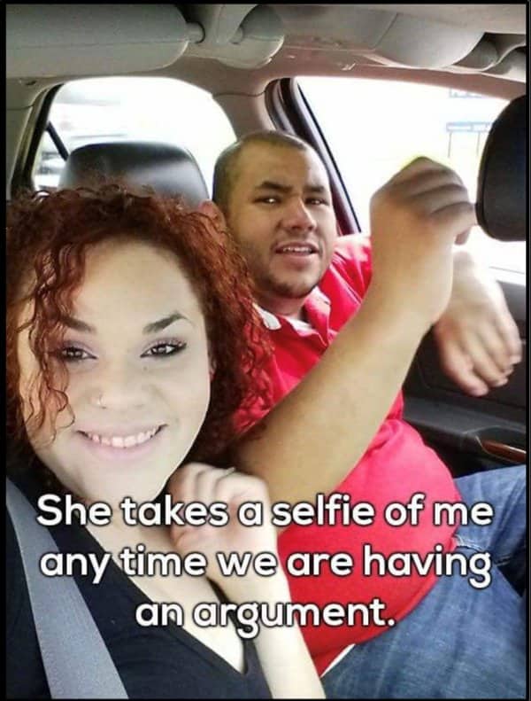 Woman grins for a car selfie while the man behind her argues in mid sentence.