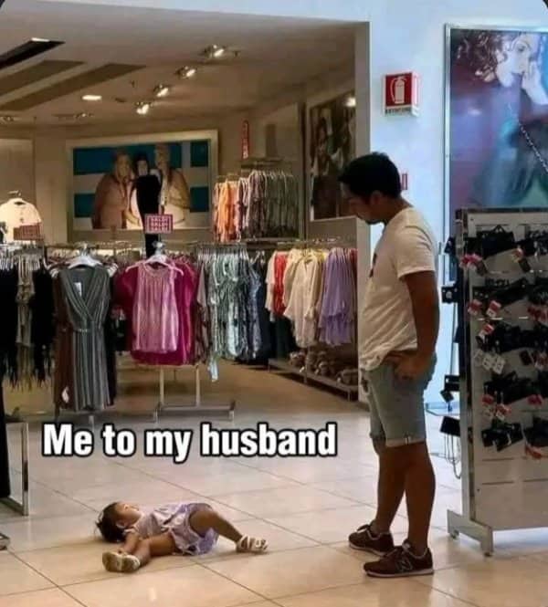 Toddler lies flat on a store floor while a man waits nearby looking entirely unimpressed.