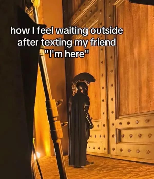 Fully armored ancient warrior waiting dramatically outside giant wooden doors after texting 'I'm here' in a meme dump.