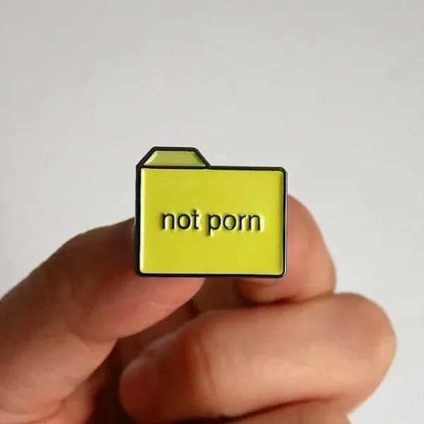 Yellow enamel folder lapel pin engraved with the words 'not porn' held between two fingers, featured in a meme dump.