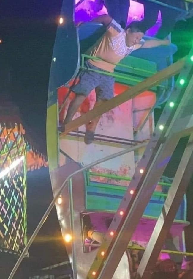 Terrifying night photo of a carnival visitor clinging frantically to the outer steel frame of an inverted swinging pirate ship ride in mid-air, shared in a meme dump.