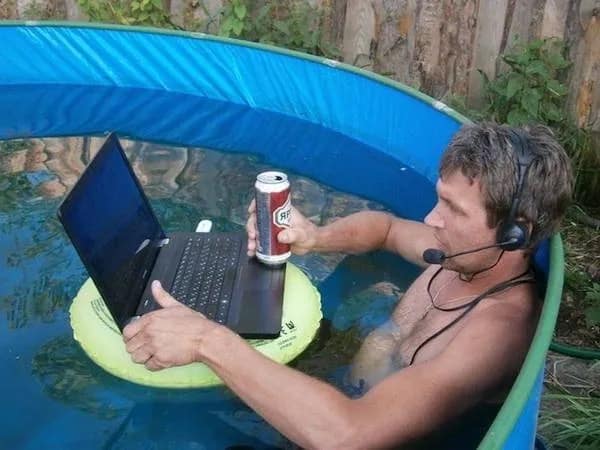 Man conducting remote work in an inflatable pool with a headset while his laptop floats on an inner tube in a meme dump.