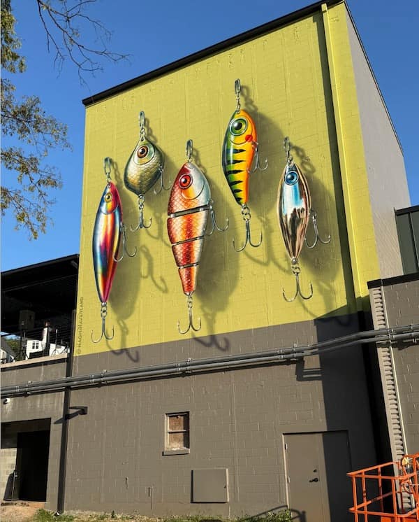 Building wall painted with a hyper-realistic 3D mural of giant fishing lures in a funny memes picture.