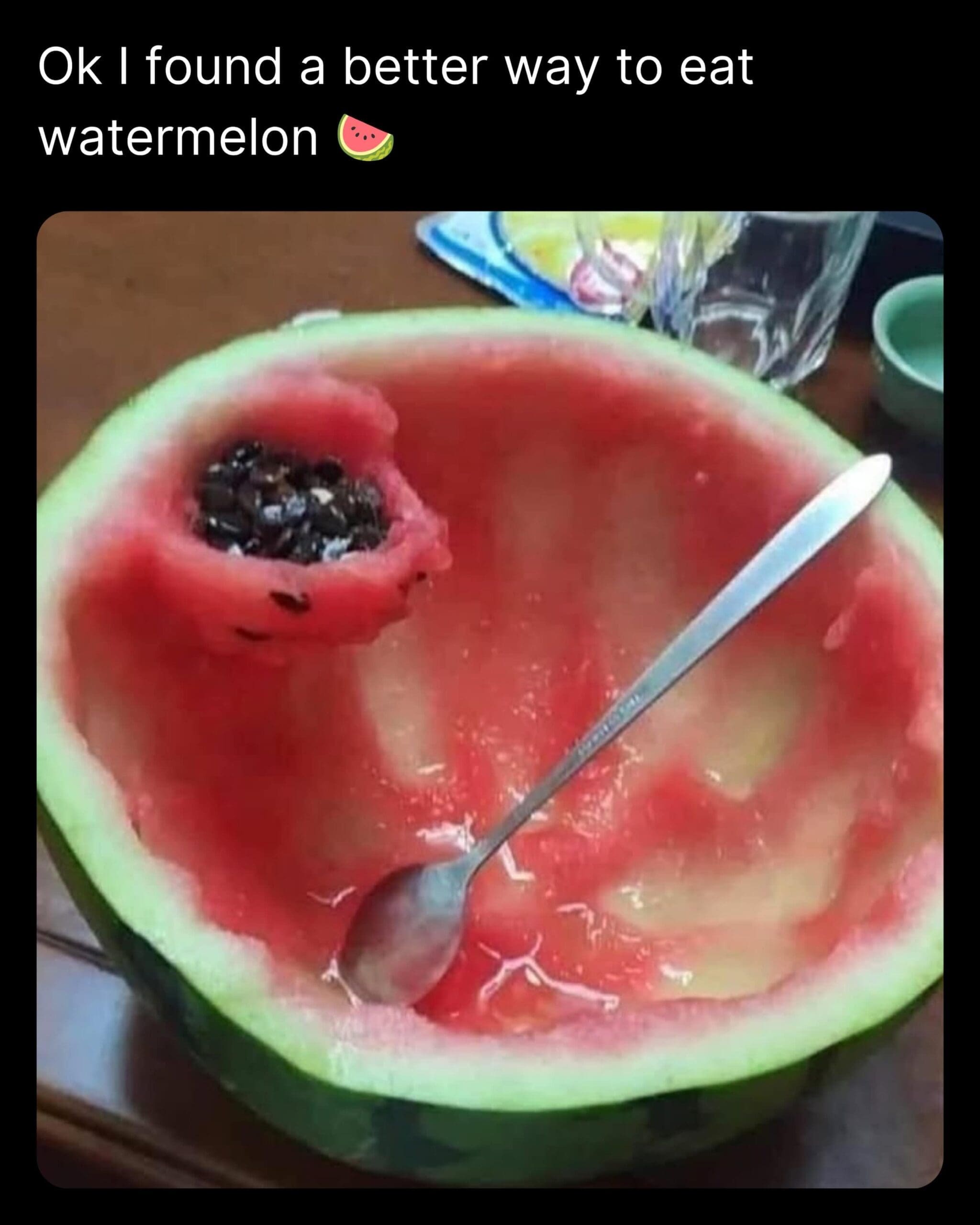 Overhead shot of an eaten watermelon half featuring a clever custom-carved flesh pocket on the rim used to hold all the discarded black seeds in a meme dump.