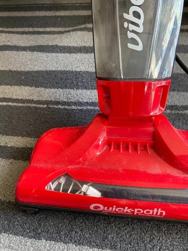 Close-up photo of a bright red carpet vacuum cleaner with a white iPhone charging cable hopelessly tangled around the roller brush in a meme dump.