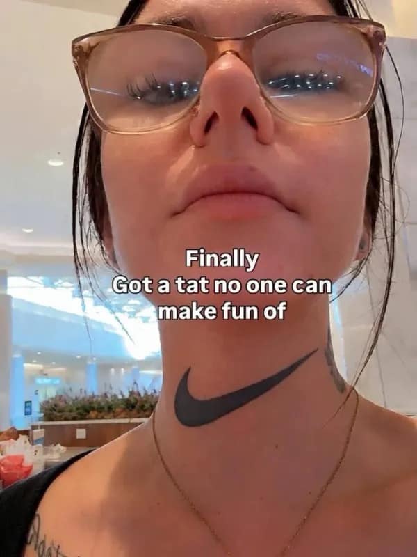Woman with glasses posing to show a black Nike swoosh logo tattooed directly across her throat, featured in a meme dump.