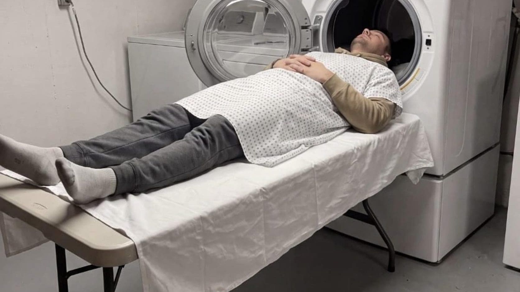 Man in a hospital gown lying on a table with his head inside a washing machine, a fake MRI from this Sunday meme dump.