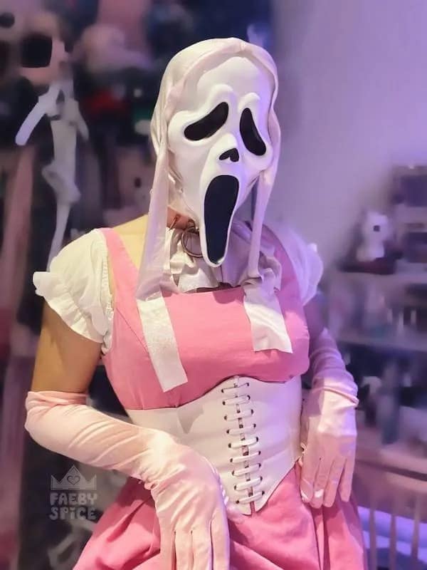 Cosplayer wearing a Ghostface mask from Scream paired with an elegant pink corset dress and silk opera gloves in a meme dump.
