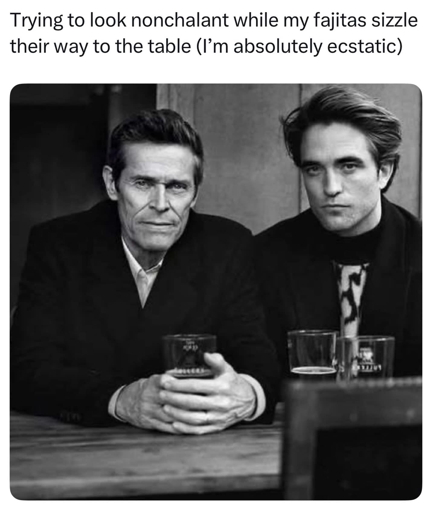 Black-and-white photo of Willem Dafoe and Robert Pattinson looking intense at a bar, captioned waiting for sizzling fajitas in a meme dump.