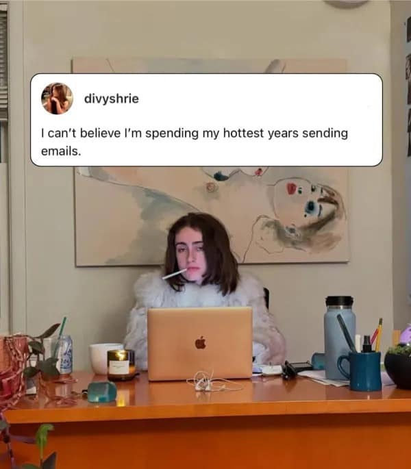Woman sitting at a desk with an unlit cigarette at her laptop, tweet-captioned about spending prime years sending emails in a meme dump.