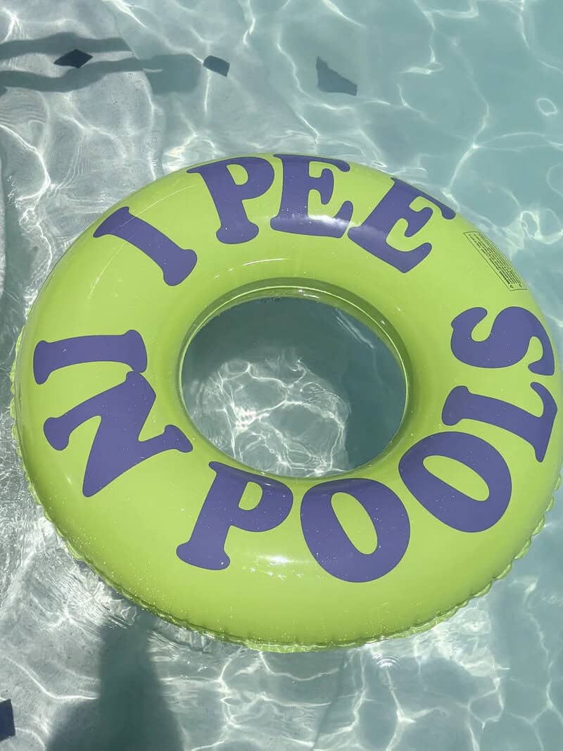Bright green inflatable pool float with bold text reading I pee in pools funny meme.