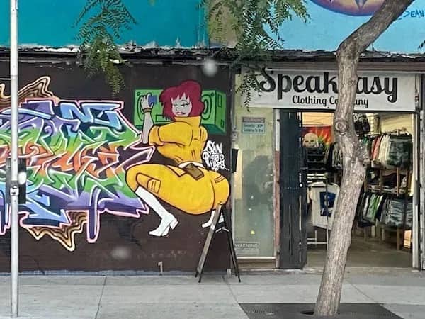 Funny memes street art featuring April O'Neil character in yellow jumpsuit next to store front.