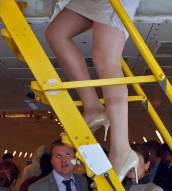 Man sitting under yellow ladder looking up at woman wearing heels funny workplace meme.