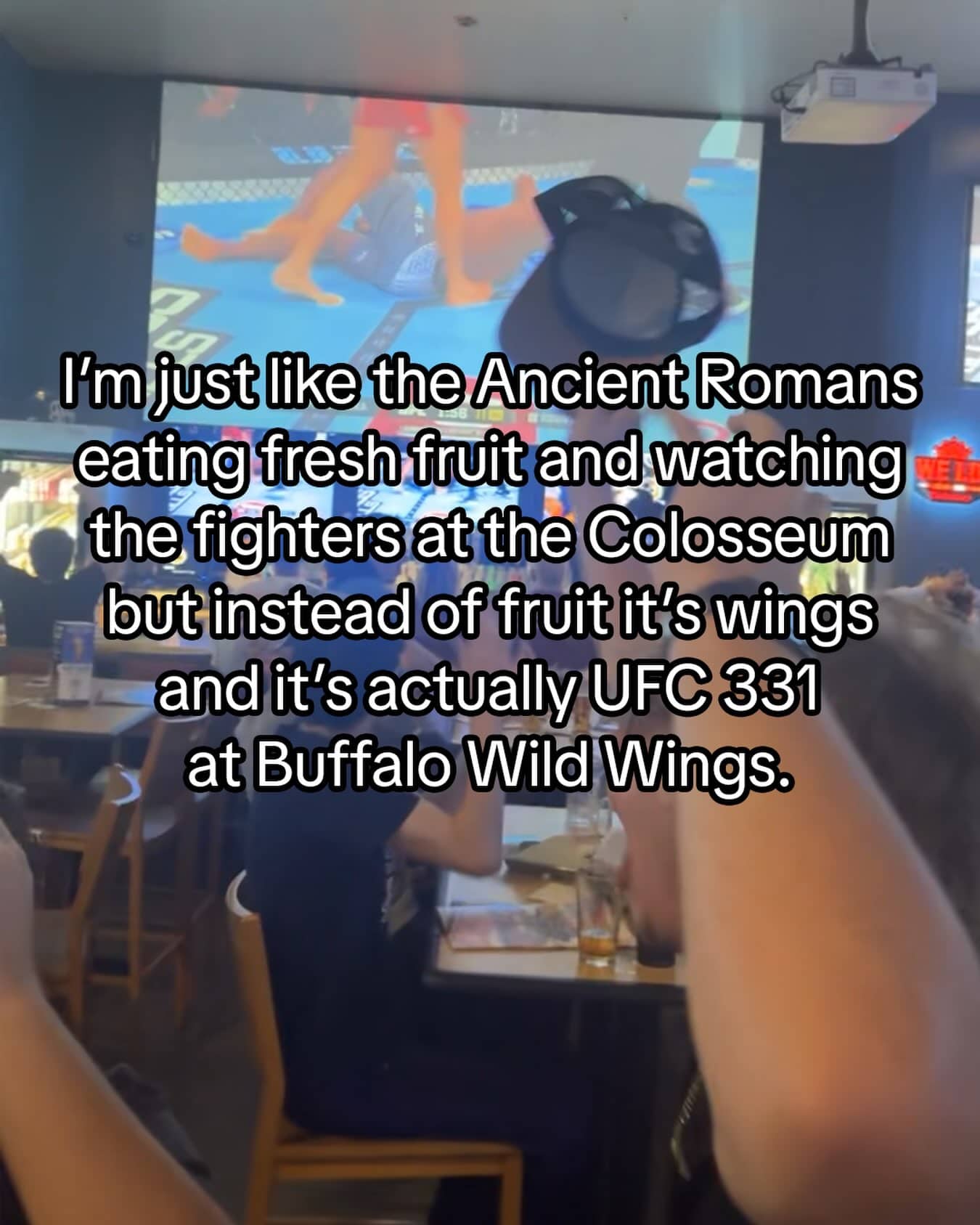 Restaurant view watching a UFC fight on a big screen with funny text overlay.