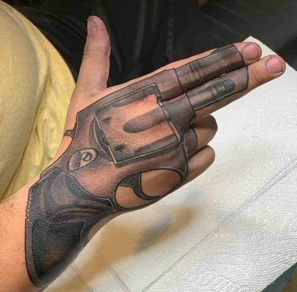 Detailed hand tattoo of a revolver pistol aligned along fingers making a gun shape.
