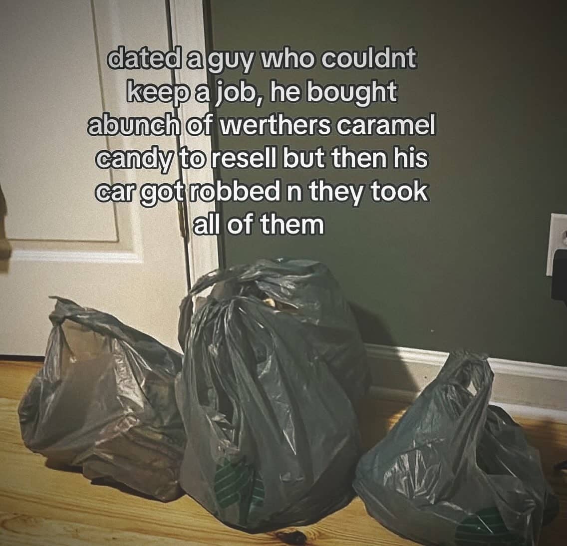 Three full plastic trash bags sitting on a wooden floor near a doorway indoors.