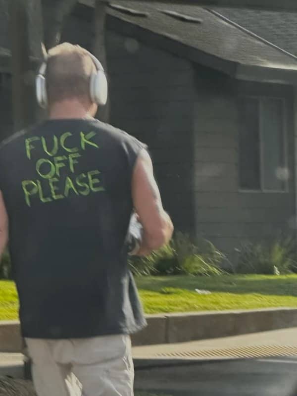Man in headphones wearing a shirt painted with a rude message ending in please