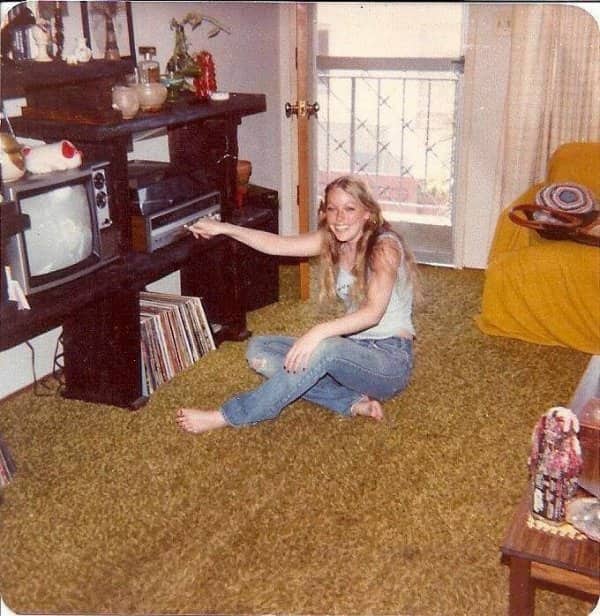 Woman sitting barefoot on thick shag carpet in vintage living room near record player.