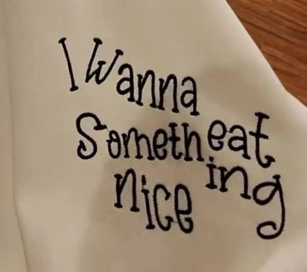 White shirt embroidered with jumbled text reading I wanna eat something nice misspelled style.
