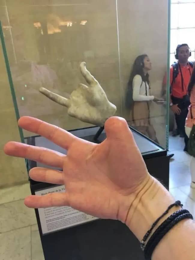 Hand posed beside a marble sculpture of a hand in a museum display case.