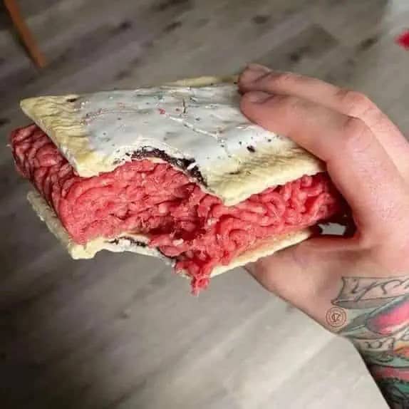 Hand holding a frosted toaster pastry sandwich stuffed with raw ground beef.